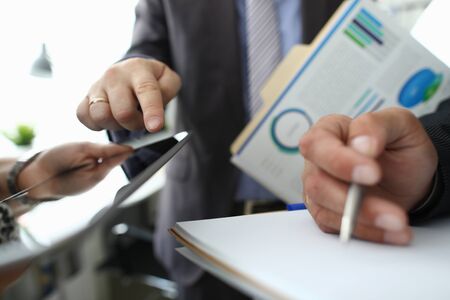 Focus on male hand pointing at tablet screen and explaining something. Colleagues holding important documents with biz charts, graphs, diagrams. Business meeting concept. Blurred backgroundの写真素材