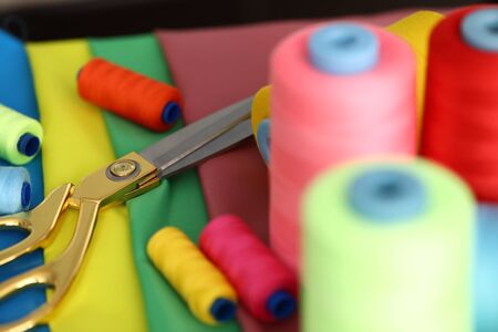 Focus on metallic beautiful scissors lying on table covered with diverse strips colorful spools of...