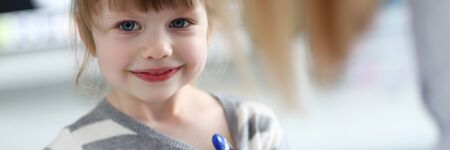 Portrait of cute little girl sitting at doctor office with thermometerの写真素材