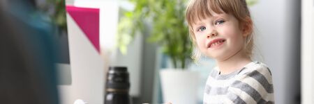 Cute little girl sitting at home at worktable looking in cameraの写真素材