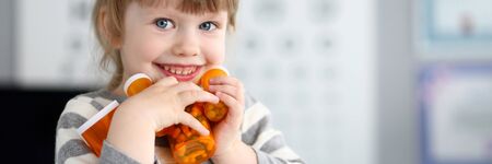 Cute smiling happy little girl grab pile of bottles with tabletsの写真素材