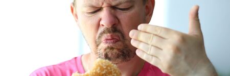 Unhappy man sniffing suspicious burger examining its freshness