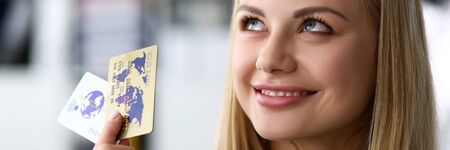 Beautiful blonde adult caucasian woman in office hold two credit cardsの写真素材