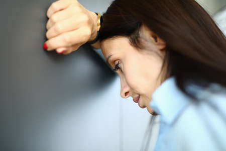 Sad woman is standing against wall with her elbow on her armの写真素材