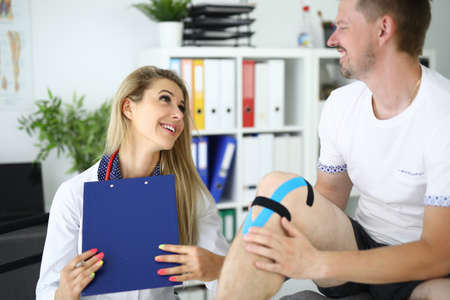 Female doctor fixed kinesio tape on patients leg.