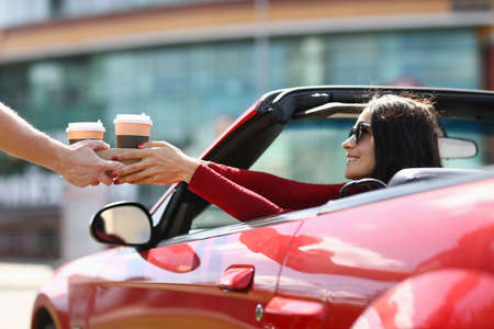 Woman in cabriolet picks up hot drinks from a courierの写真素材