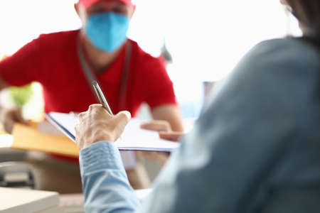 Client signs clipboard to courier wearing medical mask.