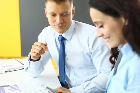 Businessman and businesswoman are sitting in office at table and looking at smartphoneの写真素材