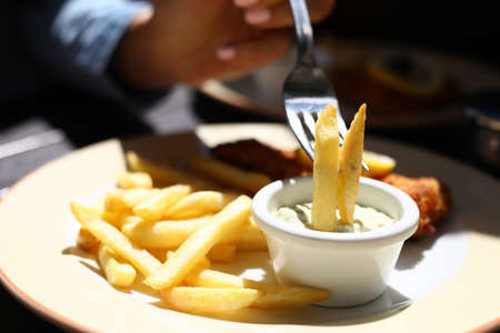 French fries on a fork in sauce next to meat chop.