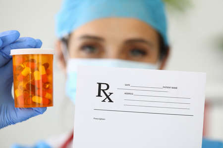 Pharmacist holds medicine and prescription in hand.