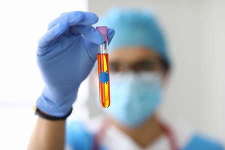 Laboratory assistant in protective mask holds flask with liquid containing bacteria.