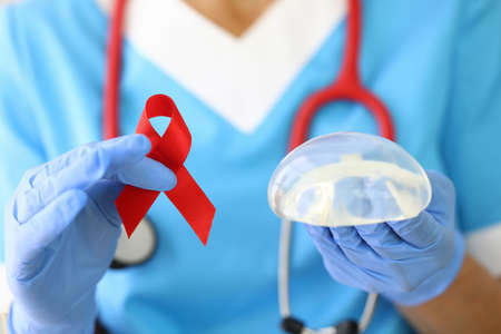 Doctor holds breast implant and red ribbon in his hand.の写真素材