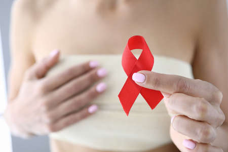 Womans hand holds red ribbon in her hand and holds other hand on her chest in bandage.
