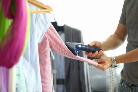 Man holds steamer in his hands and ironing shirt on hangerの写真素材
