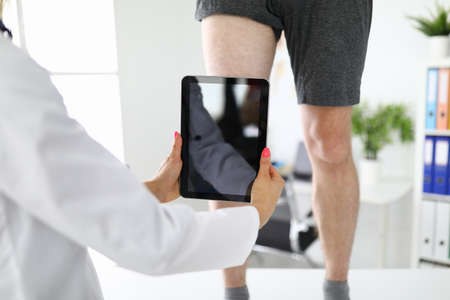 Doctor takes pictures of injured knee on tablet.
