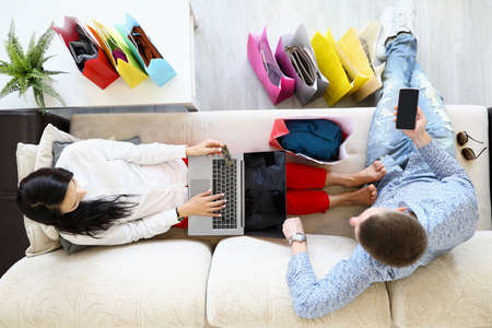 Man and woman are sitting on couch shopping online with credit cardの写真素材