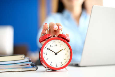 Woman in office holds a hand on red alarm clock.の写真素材