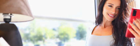 Woman is sitting in cafe smiling and looking at smartphone.の写真素材