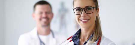 Female doctor smiling and holding clipboard from behind her colleague is standing.の写真素材