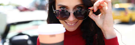 Woman in sunglasses holds hot drink in her hands