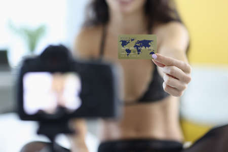 Woman in lingerie holds out bank card to camera.