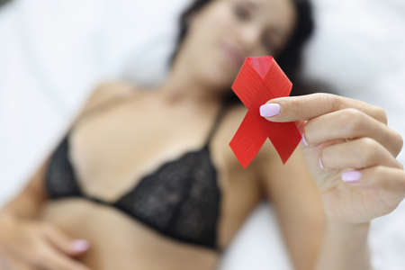 Woman is holding red ribbon while lying on t bed.の写真素材