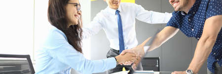 Businessmen and businesswoman in their office smiling and shaking handsの写真素材