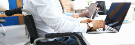 Disabled businessman sits in wheelchair in office and works at laptopの写真素材