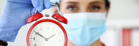 Woman doctor in protective medical mask holds an alarm clockの写真素材