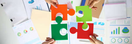 Businessmen hold multicolored puzzles in hand above table with commercial indicators.の写真素材