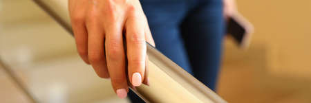 Businesswoman comes down stairs and holds on to handrailの写真素材