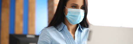 Businesswoman in protective medical mask is sitting in officeの写真素材