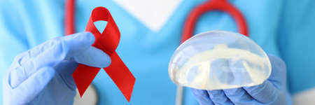 Doctor holds breast implant and red ribbon in his hand.の写真素材