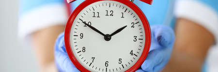 Doctors hands in gloves hold red alarm clock.の写真素材