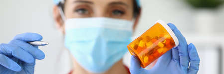 Woman doctor in mask holds jar of medicines and pen in her handの写真素材