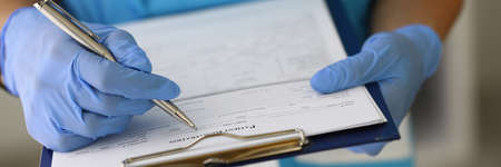 Doctors gloved hands hold clipboard with pen and patient registration document.
