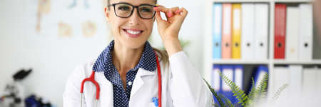 Woman doctor with glasses smiling at workplace in medical officeの写真素材