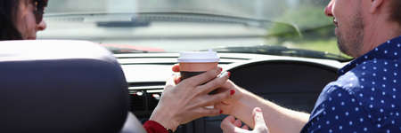 Man and woman sit in car and hold glass of drink togetherの写真素材