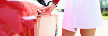 Woman stands next to red car hand on doorknob.の写真素材