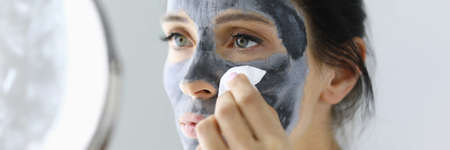 Woman looks in mirror and rinses off cosmetic mask.の写真素材