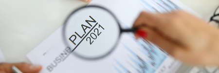 Womans hand holds magnifying glass over business plan for 2021の写真素材