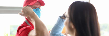 Courier wearing protective medical mask greets client safely.の写真素材