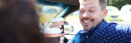 Man and woman are sitting in car and drinking coffeeの写真素材