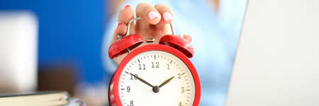 Woman in office holds a hand on red alarm clock.の写真素材