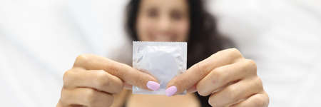 Woman holding condom while lying in bed.の写真素材