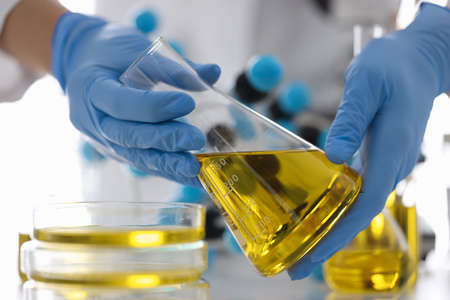 Hands in rubber gloves hold flask with yellow liquid in chemical laboratory closeupの写真素材
