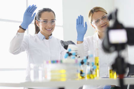Young women in white uniforms wave their gloved hands in front of camera in chemical laboratoryの写真素材