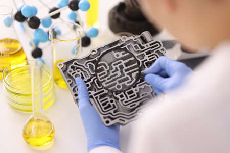 Hands in rubber gloves hold magnifying glass over automatic transmission in laboratoryの写真素材