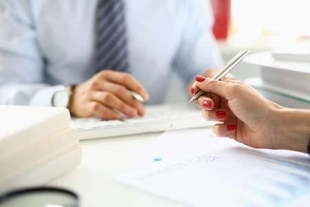 Female hand holds ballpoint pen over documents closeup in front of man in background in officeの写真素材