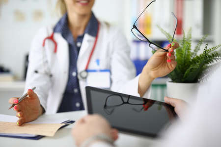 Doctors with tablet and glasses in hands are sitting at table at meeting in clinic closeupの写真素材